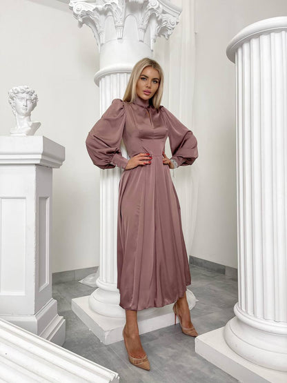 Woman in a mauve dress standing in an elegant interior setting with white columns.