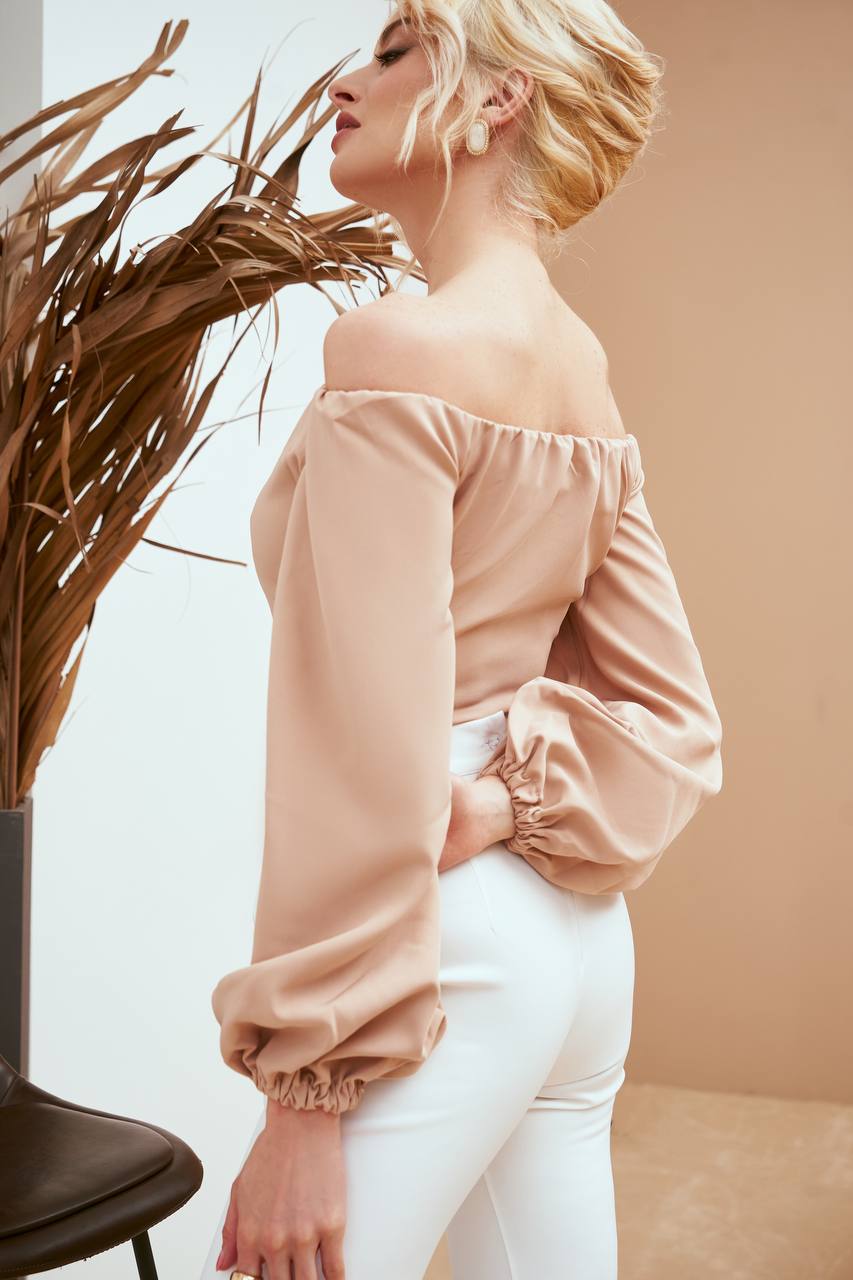 Woman wearing a light pink off-shoulder top and white pants against a neutral background