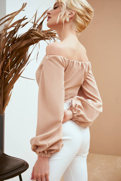 Woman wearing a light pink off-shoulder top and white pants against a neutral background