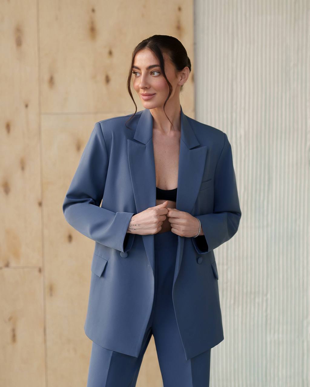 Woman wearing a blue suit standing against a wooden wall.