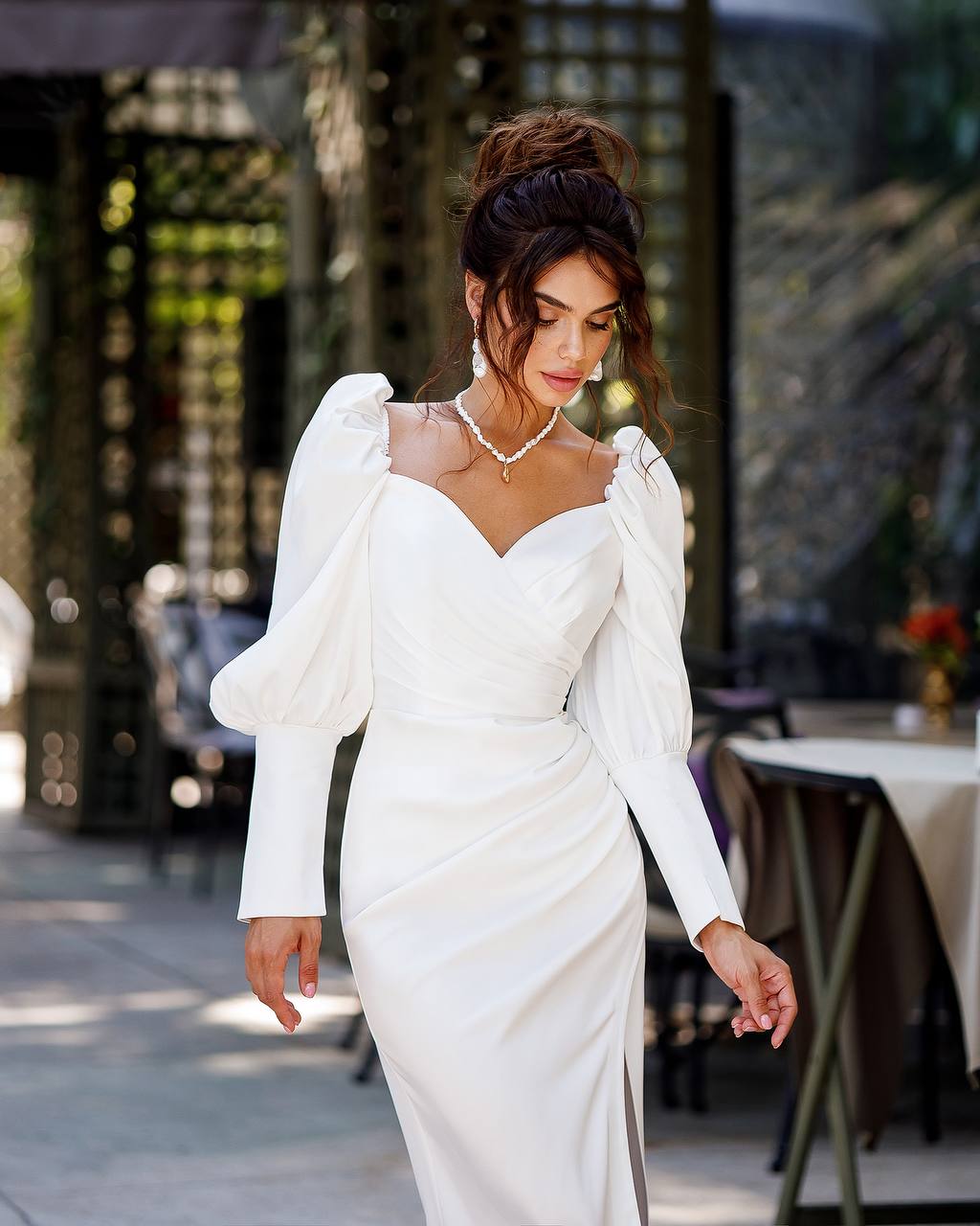 Woman in a white wedding dress with puffed sleeves standing outdoors.
