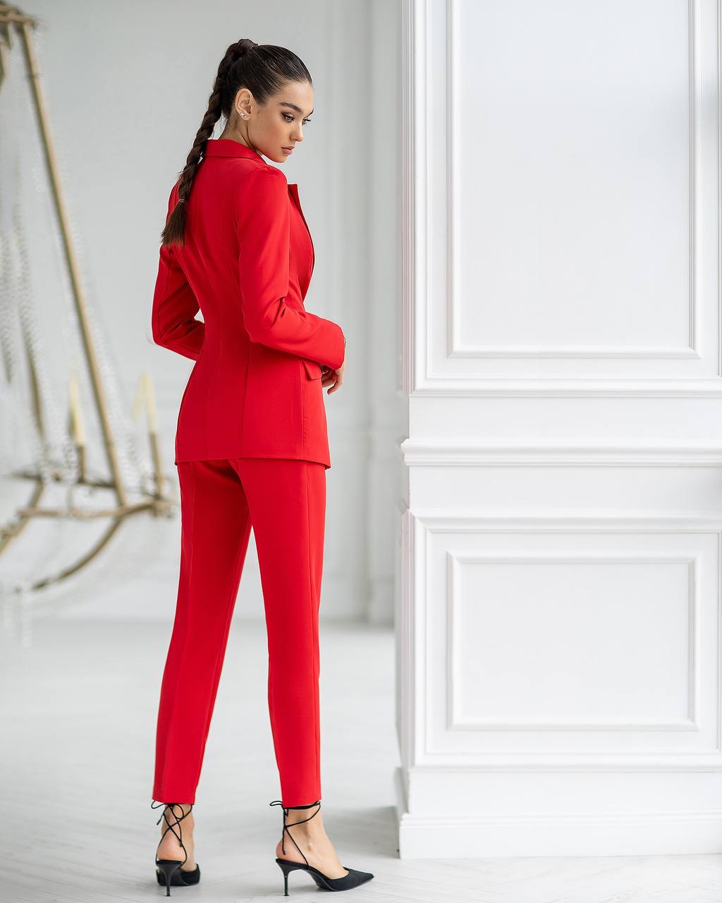 Woman wearing a red suit standing against a white wall.