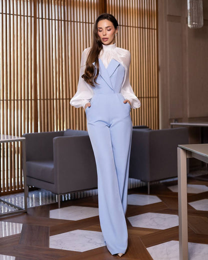Woman in a light blue suit and white blouse standing in an indoor setting with wooden flooring and furniture.