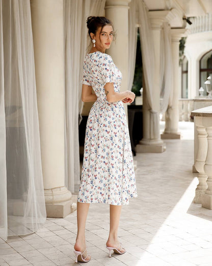 Woman in a floral dress standing in an elegant outdoor setting with columns and white curtains.