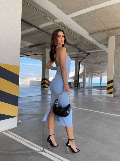 Woman in a blue dress holding a black handbag in an underpass.