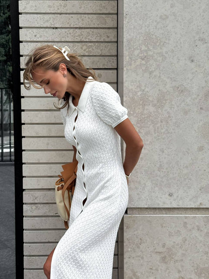 Woman in a white dress standing against a light gray wall.