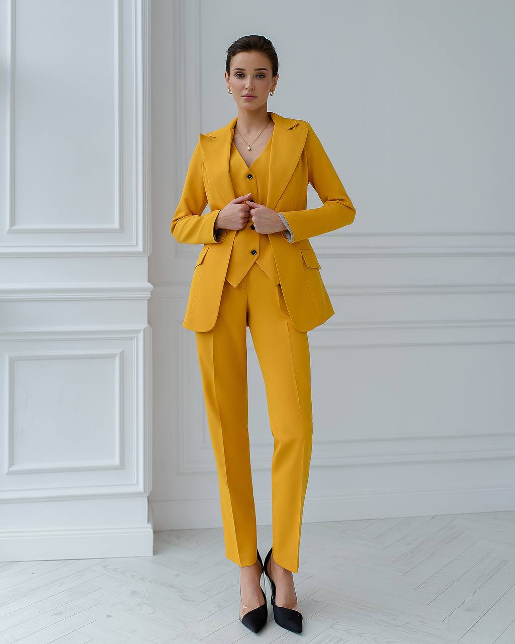 Woman wearing a yellow suit standing against a white wall.