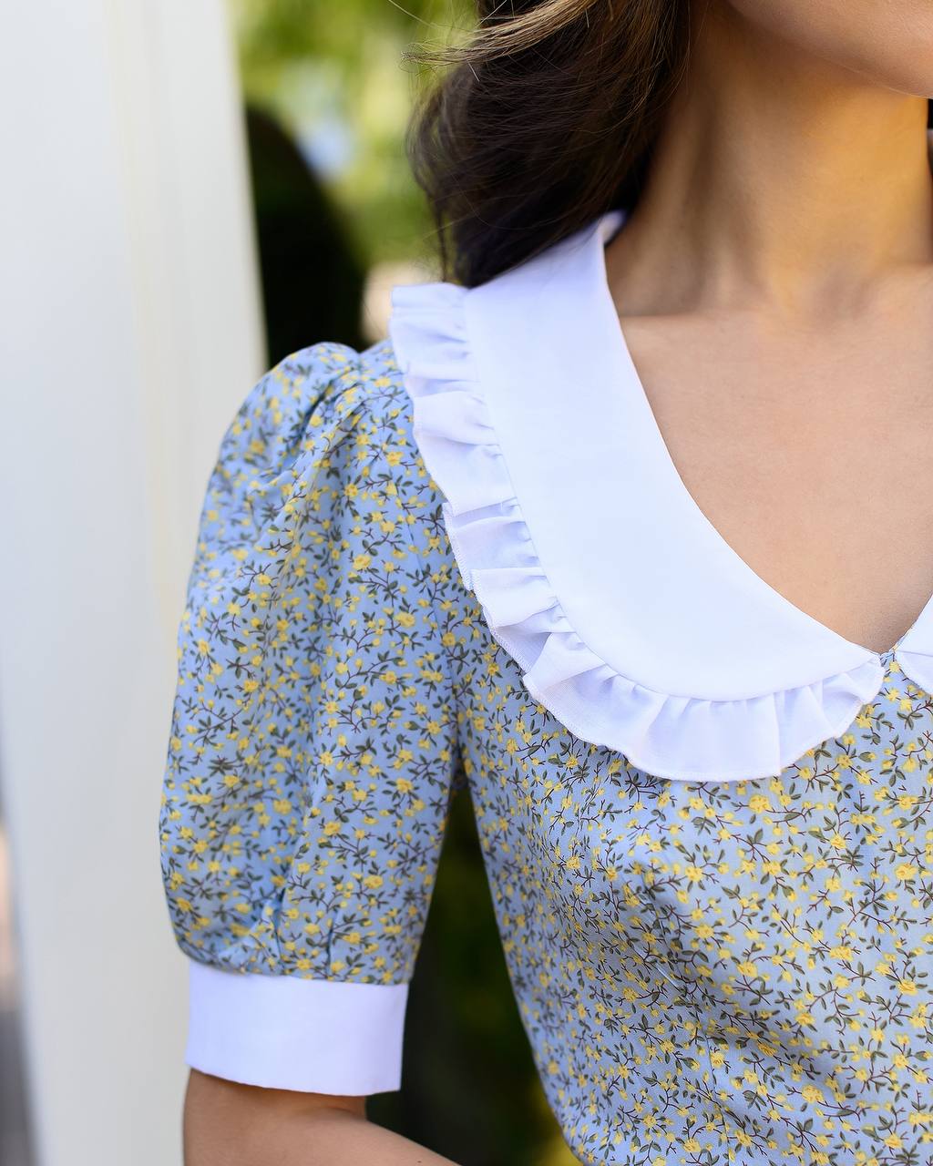 Close-up of a person wearing a floral blouse with a white collar.