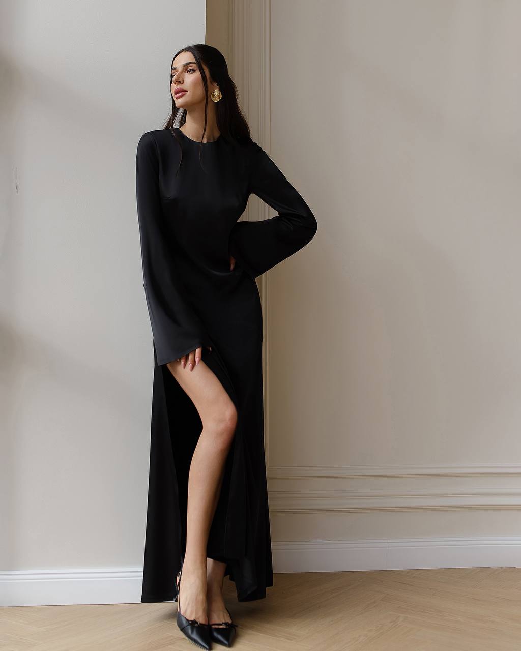 Woman wearing a black dress with a high slit in a room with beige walls.