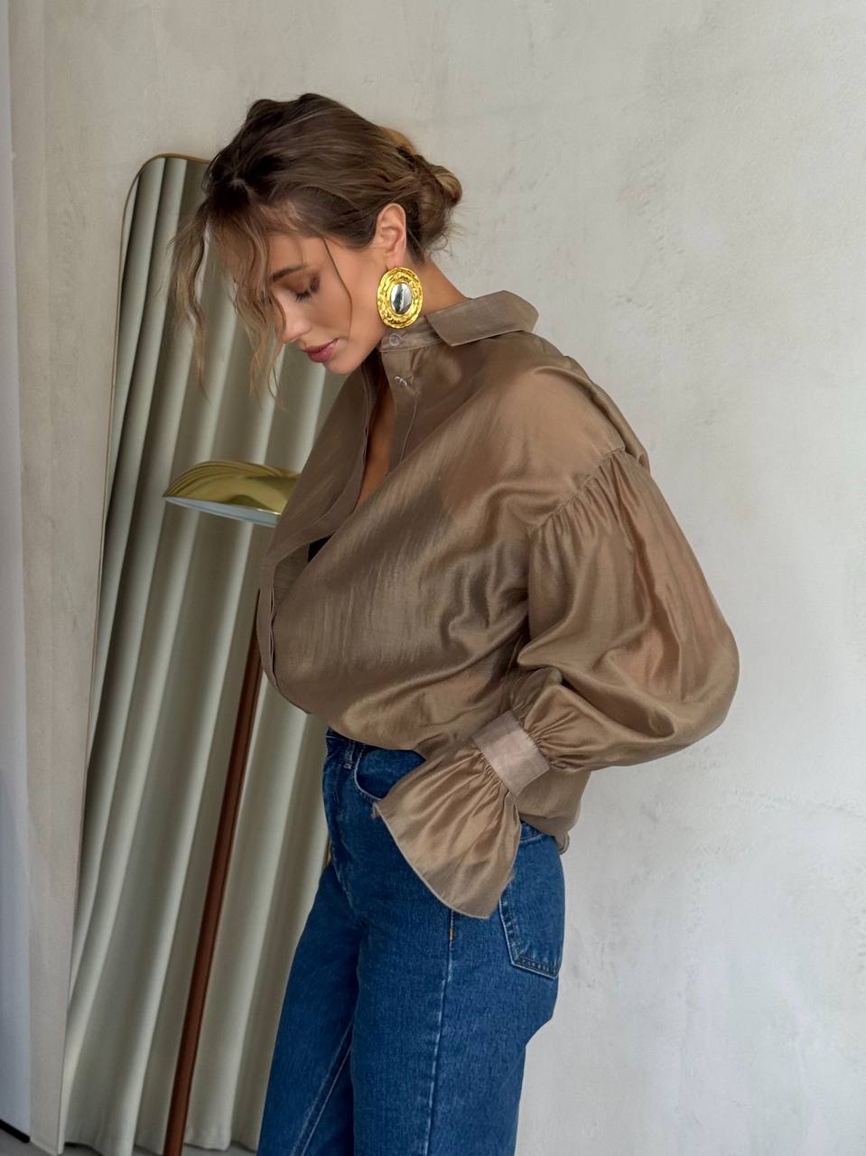 Woman wearing a beige blouse and blue jeans with a neutral background