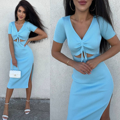 Woman wearing a light blue dress with cut-out design and side slit, standing against a white wall.
