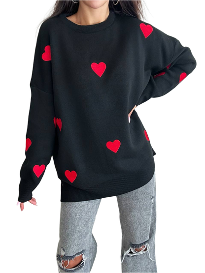 Black sweater with red heart patterns worn by a person on a white background