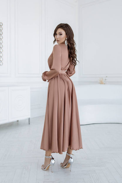 Woman wearing a long, light brown dress in a minimalistic setting