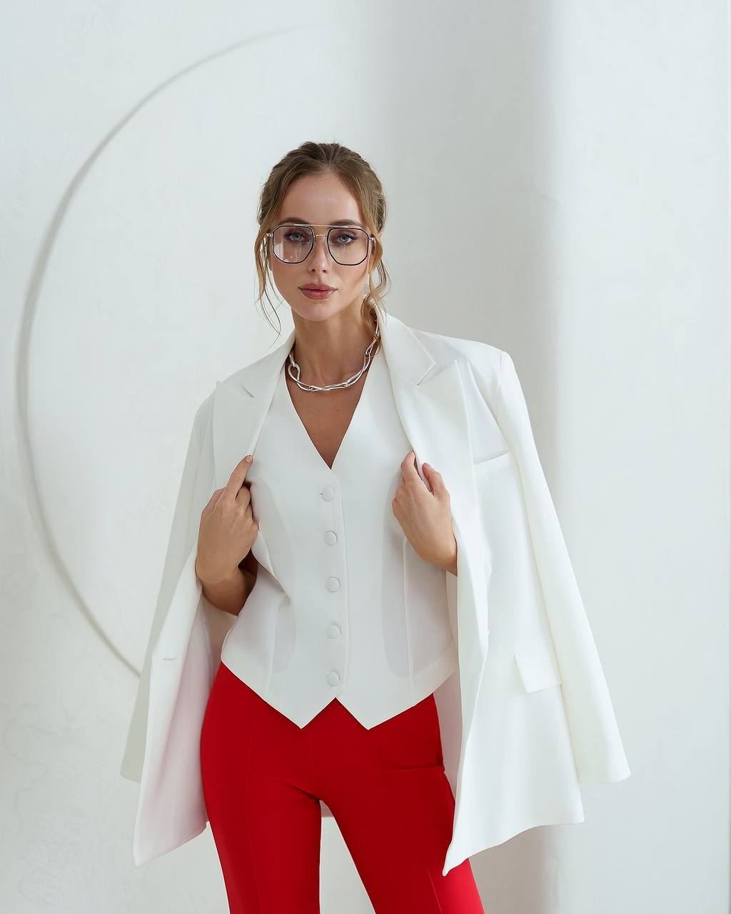 Woman wearing a white blazer over a white top and red pants on a white background