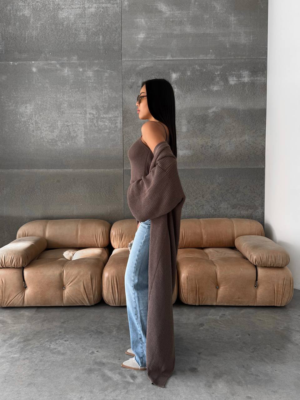 Woman standing in a modern living room with a brown sofa and gray wall.