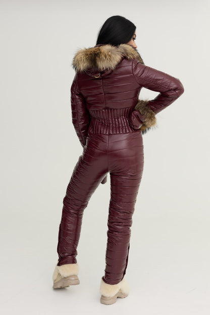 Person wearing a burgundy quilted jumpsuit with fur trim on a white background