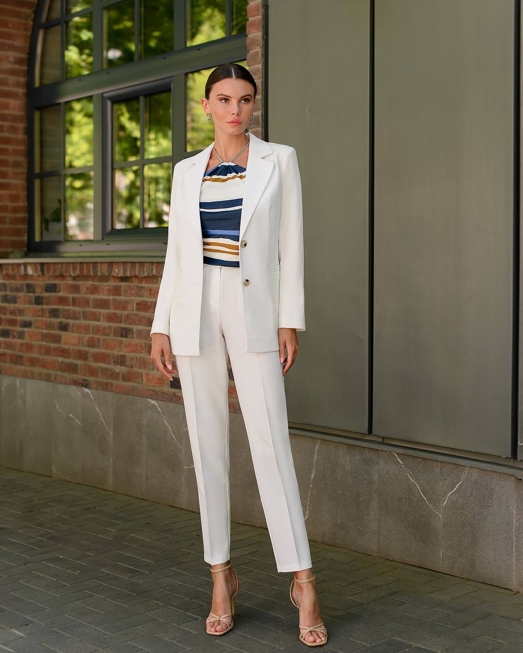 Woman in a white suit standing in front of a building with large windows.