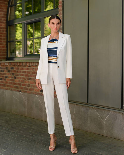 Woman in a white suit standing in front of a building with large windows.