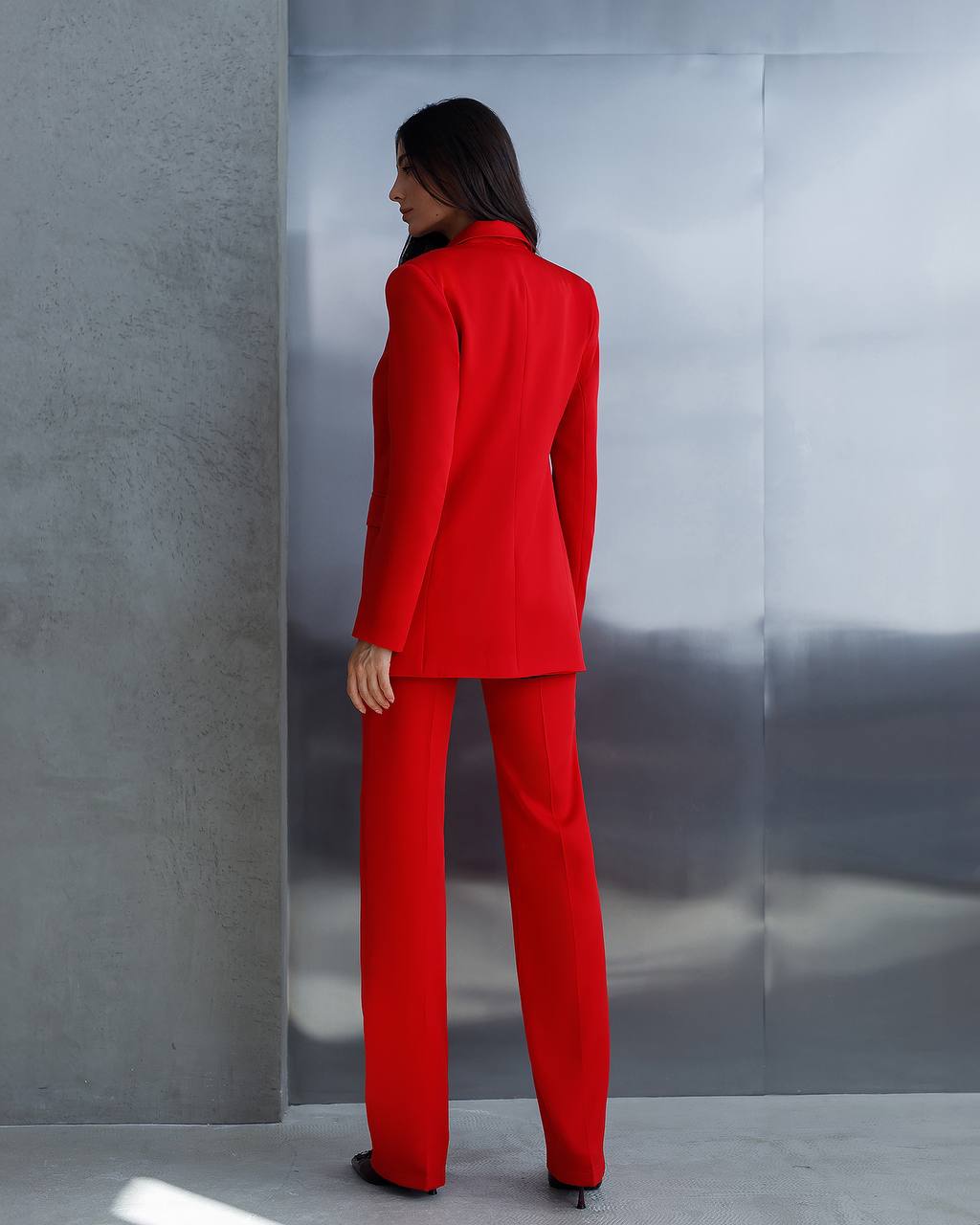 Person wearing a red suit standing against a reflective silver wall.