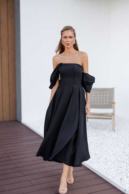 Woman wearing a black off-shoulder dress on a wooden deck.