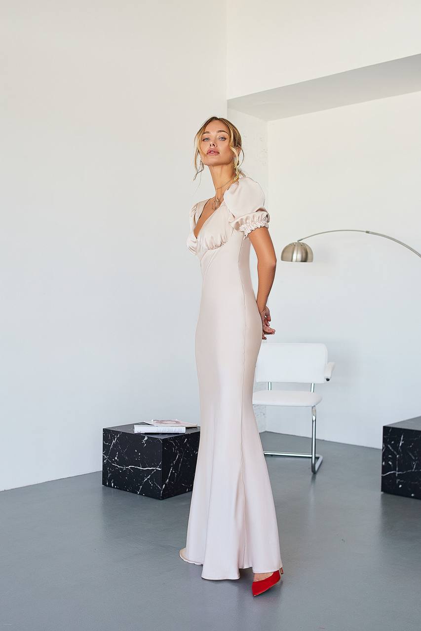 Woman in a white evening gown standing in a modern room with a white wall and gray floor.