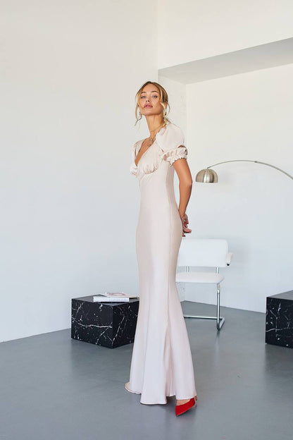 Woman in a white evening gown standing in a modern room with a white wall and gray floor.