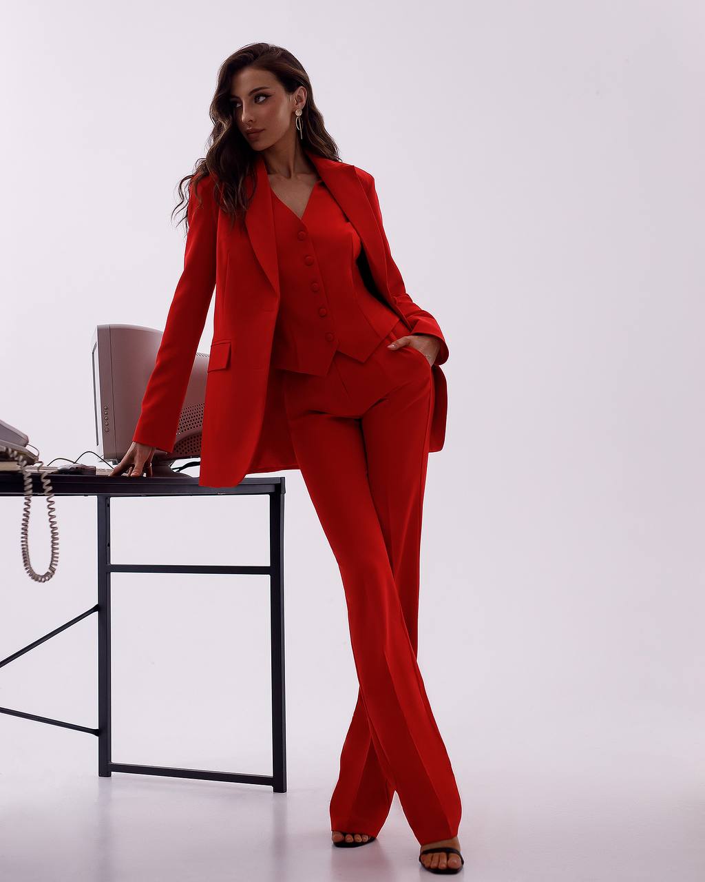 Woman in a red suit standing next to a desk on a white background