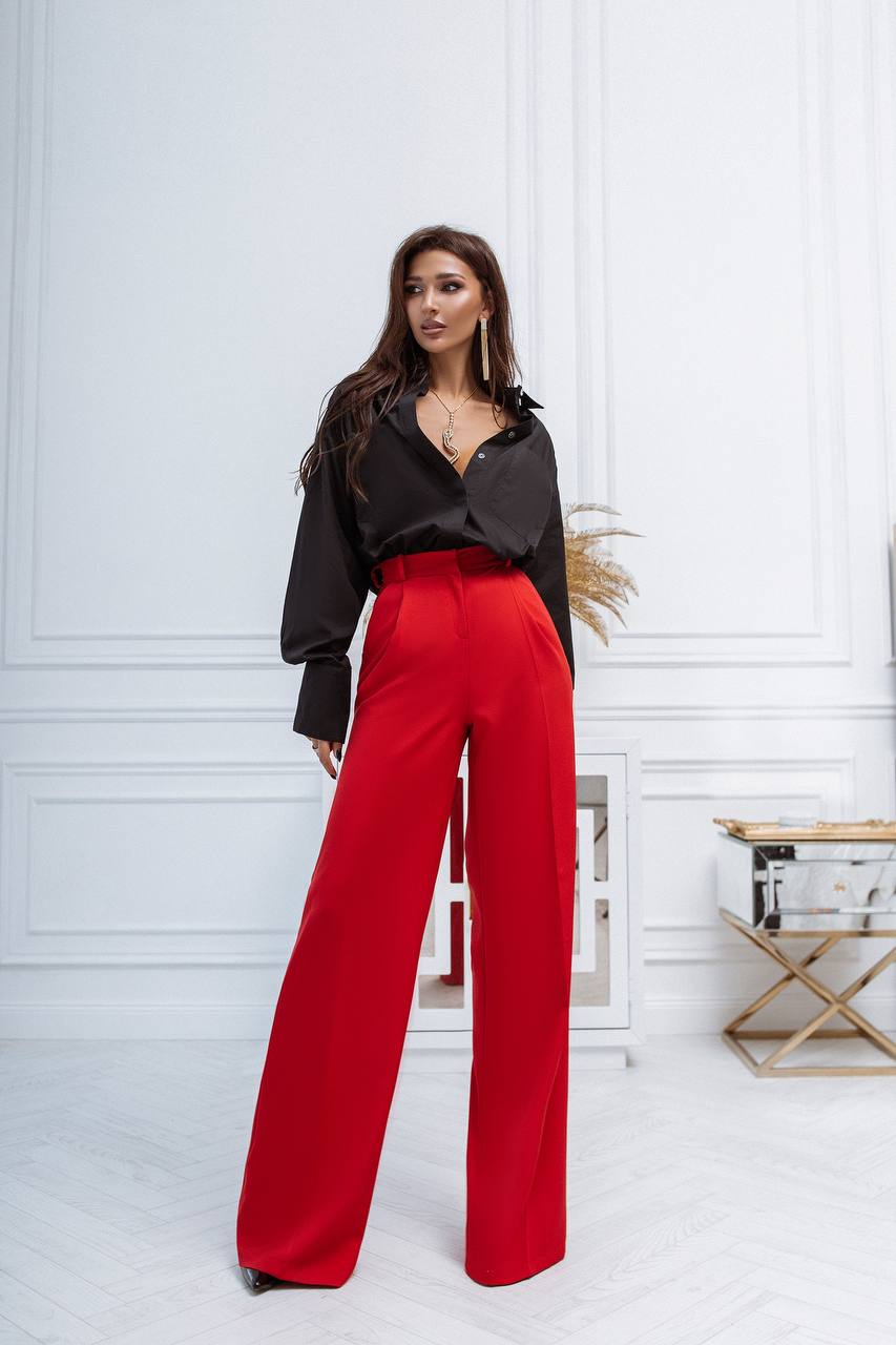 Woman wearing a black top and red pants in a minimalistic room.