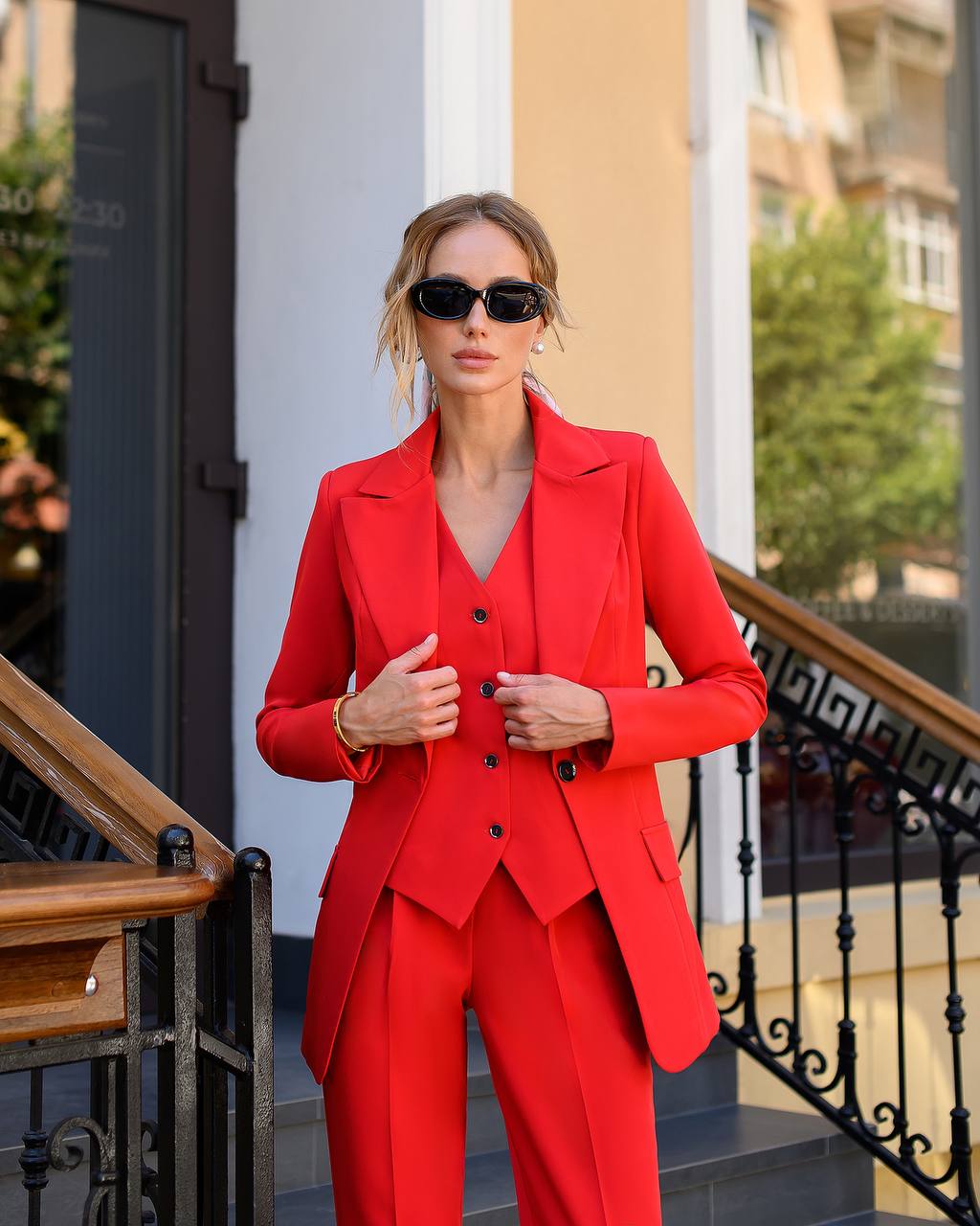 Woman in a red suit standing outdoors with buildings in the background
