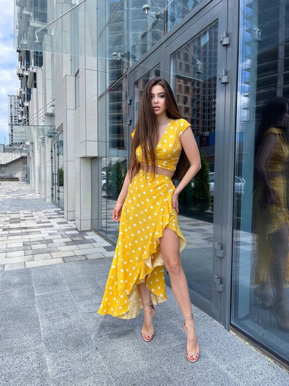 Woman in a yellow polka dot dress standing in front of a modern building.