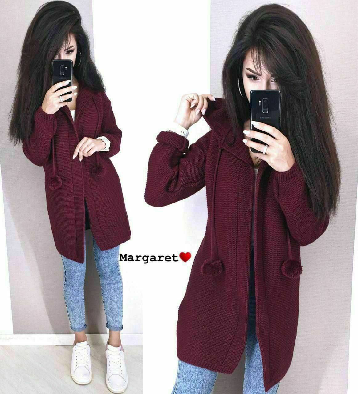 Woman wearing a burgundy coat with pom-pom details, taking a mirror selfie.