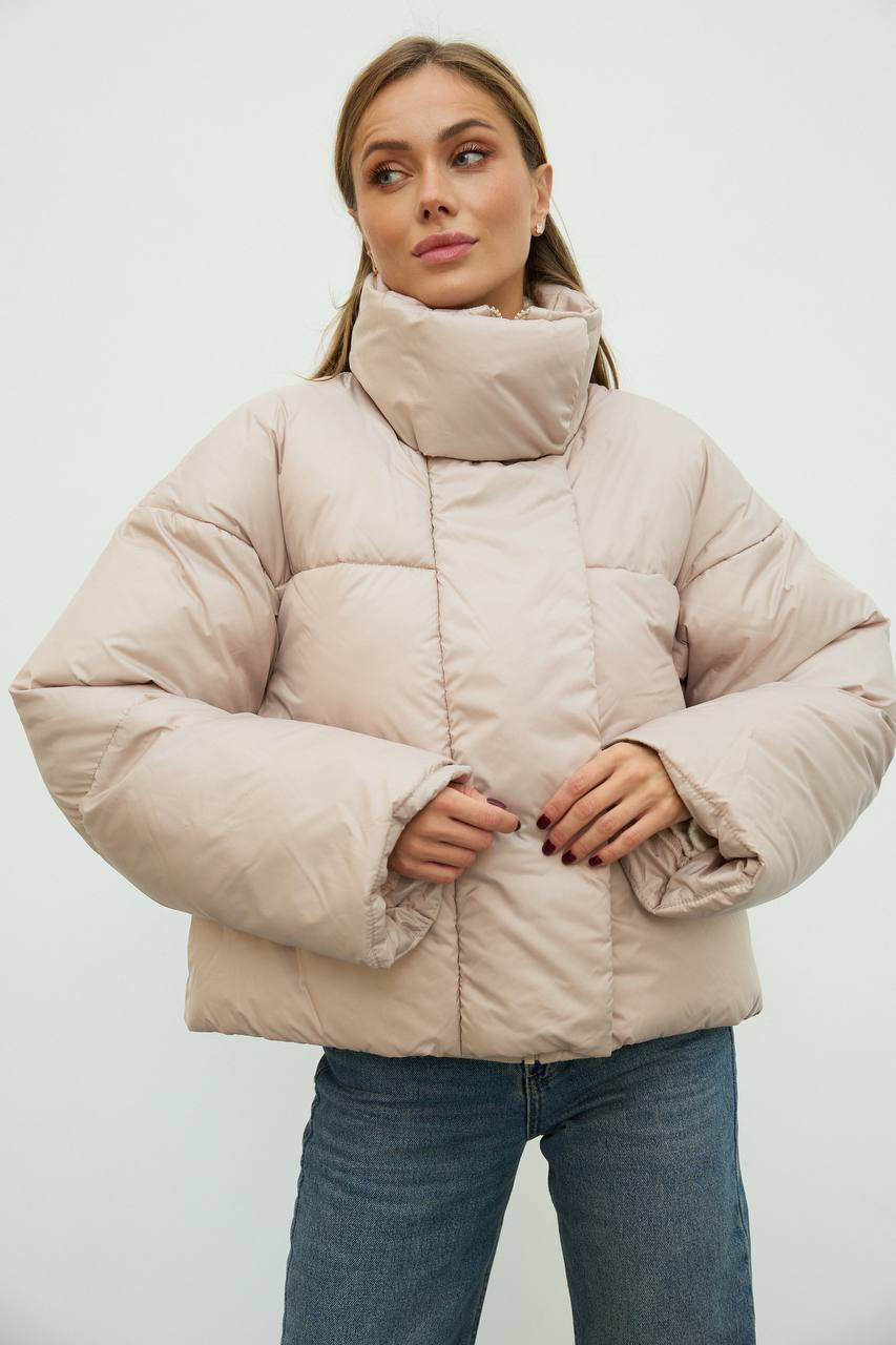 Woman wearing a beige puffer jacket against a white background
