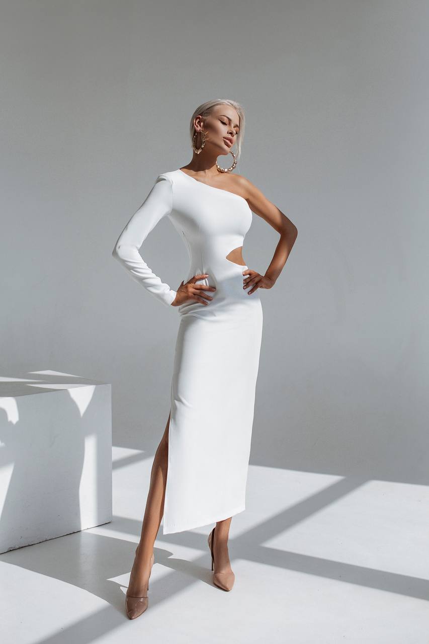 Woman wearing a white one-shoulder dress with a slit, standing against a gray background.
