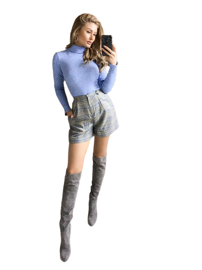 Woman wearing a blue turtleneck, plaid shorts, and gray knee-high boots on a white background