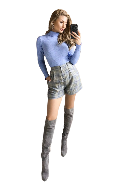 Woman wearing a blue turtleneck, plaid shorts, and gray knee-high boots on a white background