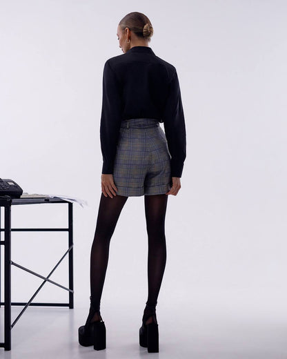 Person wearing a black top and plaid shorts on a white background