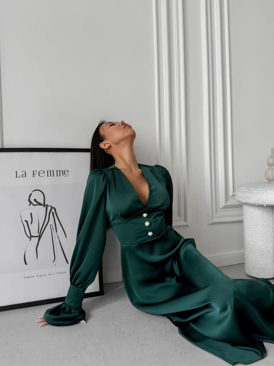 Woman in a green dress sitting on the floor against a white wall with a framed picture.