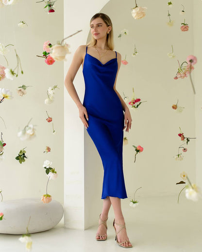 Woman in a blue dress standing against a light-colored wall with decorative flowers.