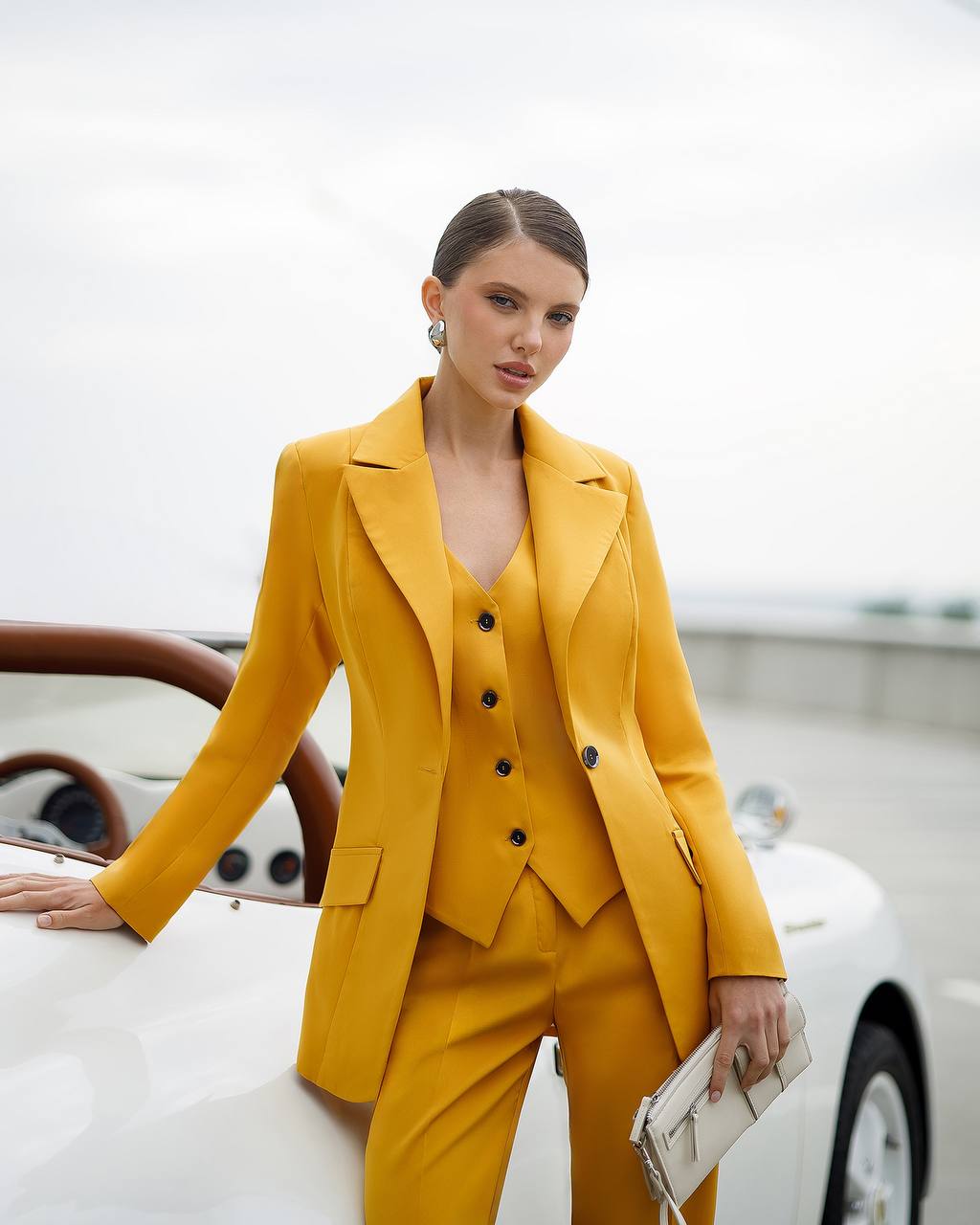 Woman in a yellow suit standing next to a white car with a blurred background
