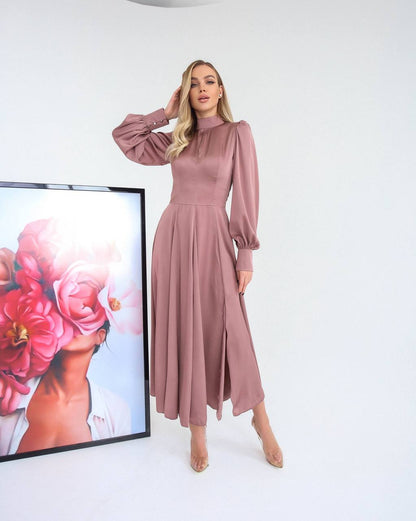 Woman in a pink dress standing next to a framed artwork of flowers on a white wall.