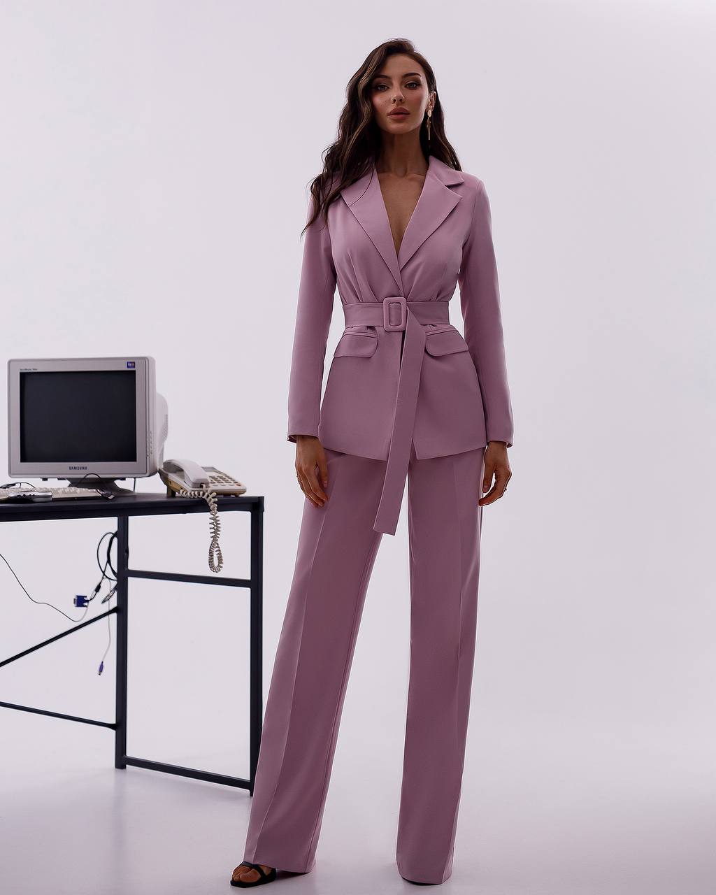 Woman in a lavender suit standing in front of a vintage computer setup on a white background