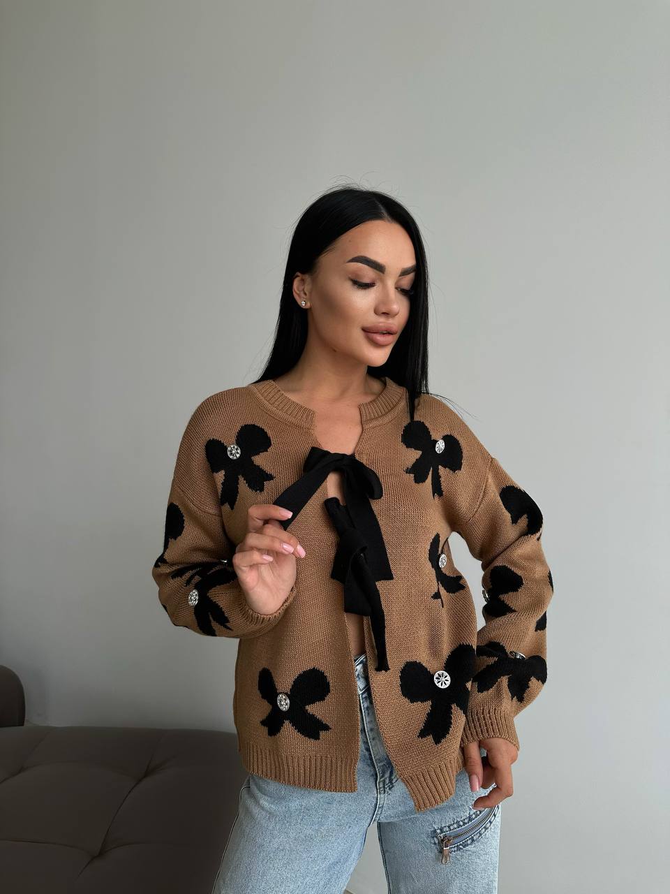 Woman wearing a brown sweater with black bow designs against a plain background