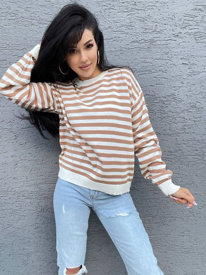 Woman wearing a striped sweater and jeans against a gray wall