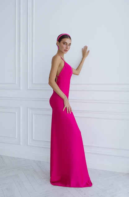 Woman wearing a bright pink evening gown against a white wall.