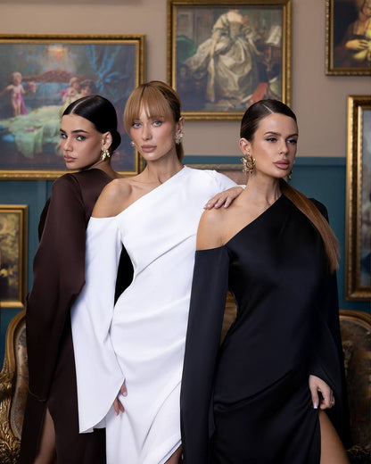 Three women in elegant dresses standing together with classical paintings in the background
