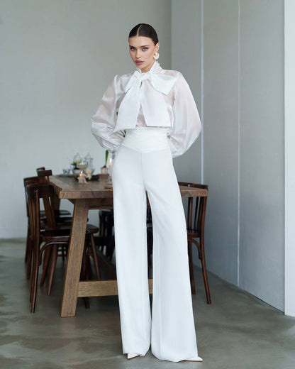 Woman in a white outfit standing in a room with a wooden table and chairs.
