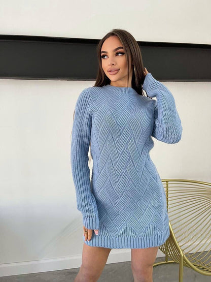 Woman wearing a light blue knitted sweater dress against a white wall.