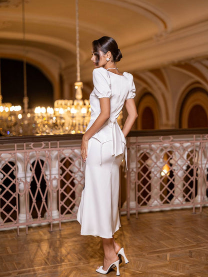 Woman in a white dress standing in an elegant indoor setting with chandeliers.