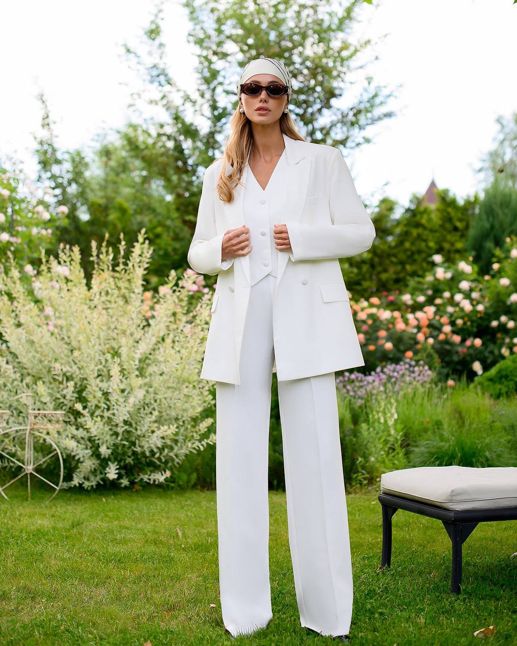 Woman in a white suit standing in a garden with greenery and flowers in the background