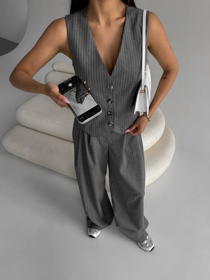 Person wearing a gray pinstripe vest and pants set, holding a phone.